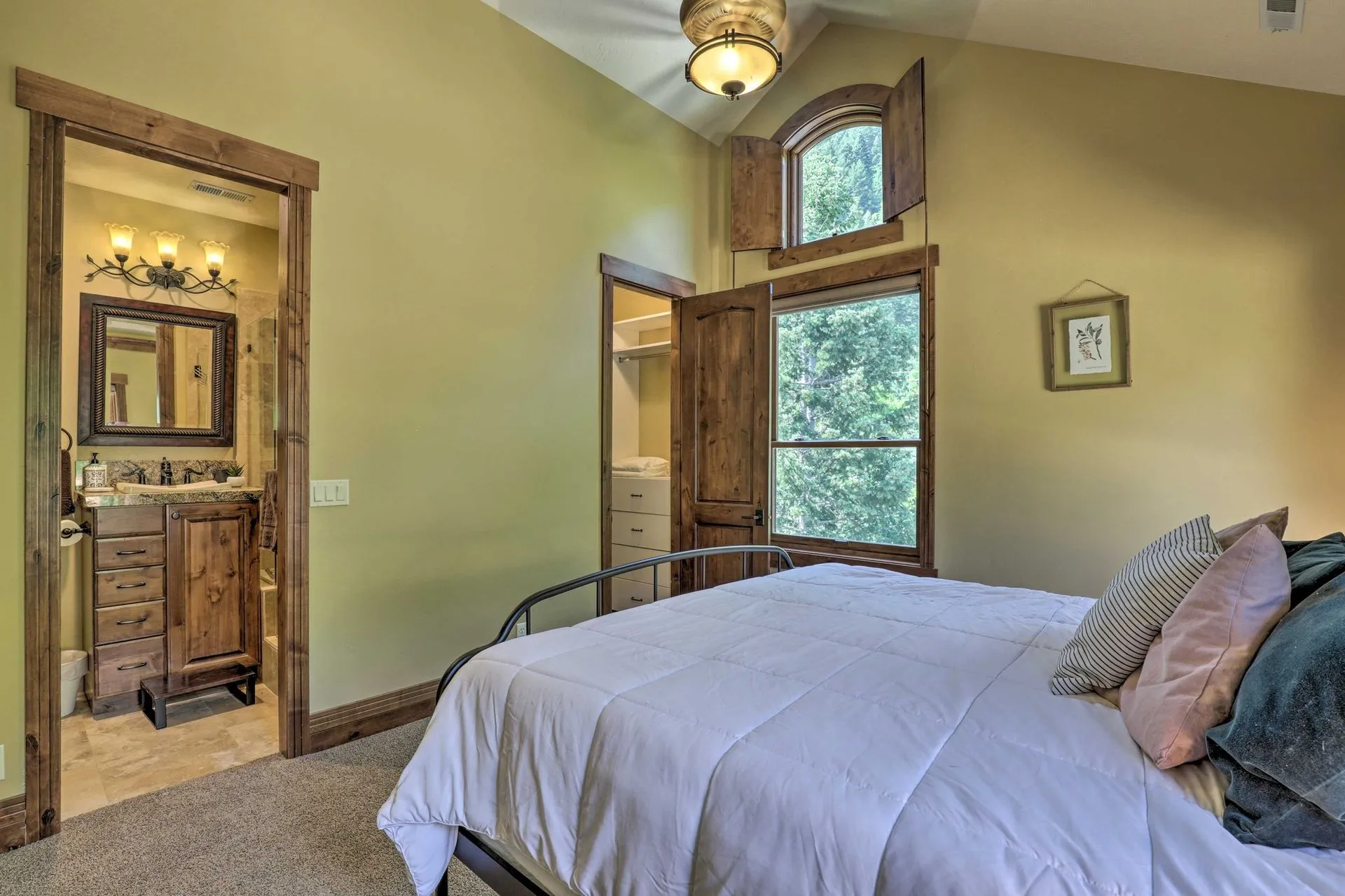 Primary bedroom with king bed, ensuite bathroom, and forest views through arched windows